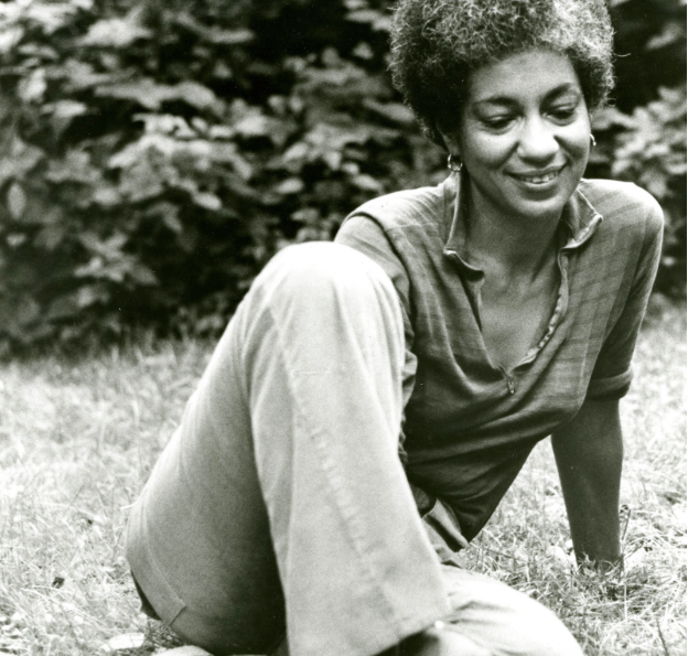 June Jordan sitting on lawn looking down and smiling