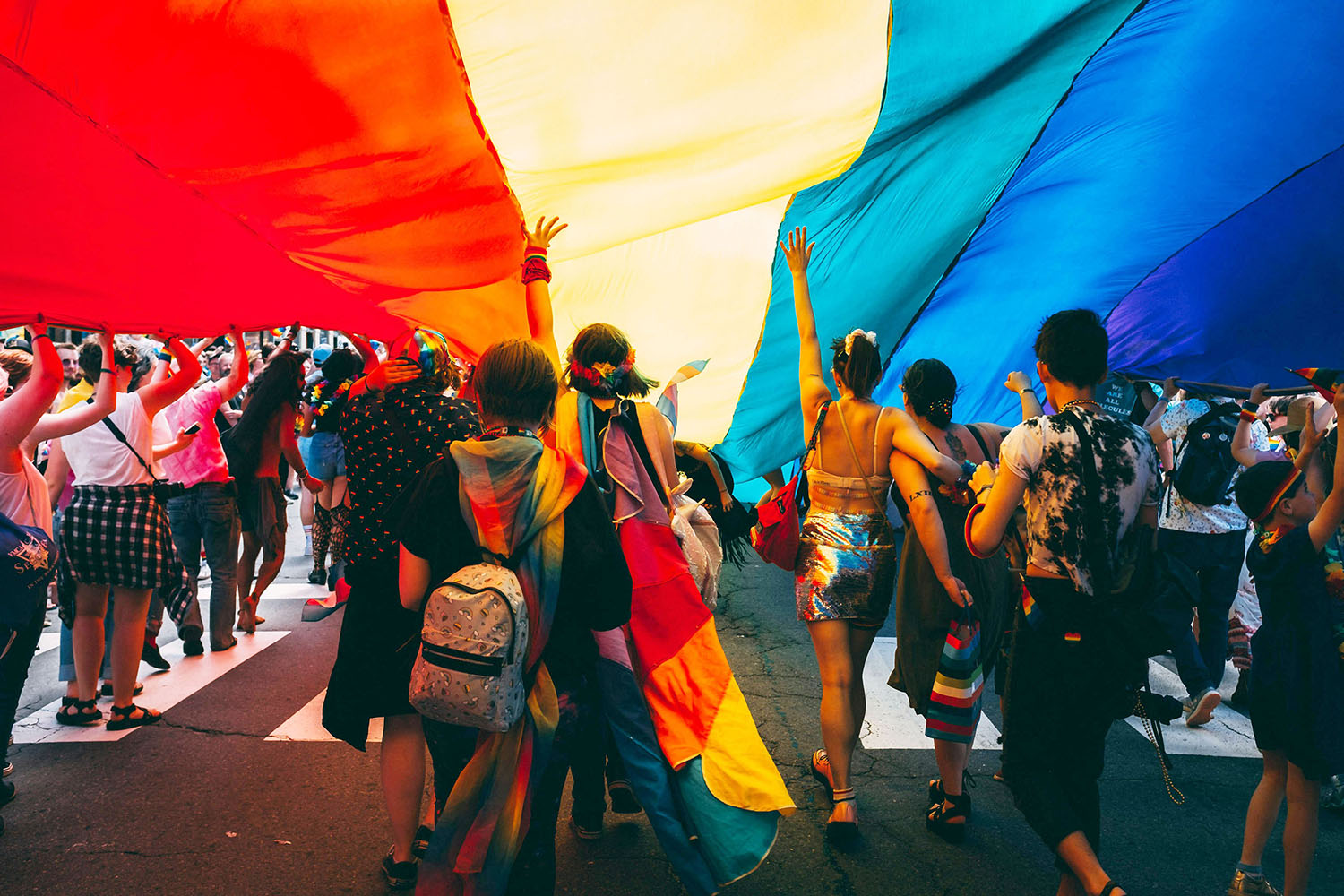 People marching under a huge LGBTQ flag