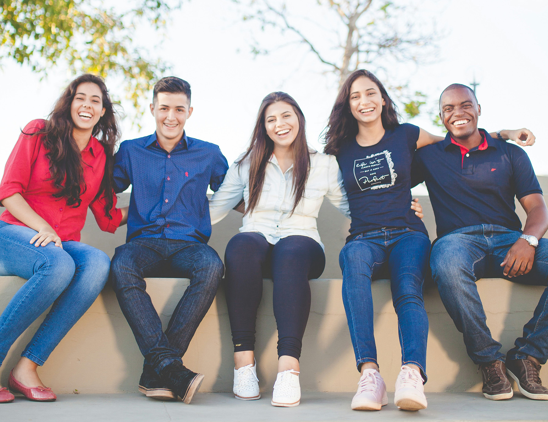 Group of students sitting on a wall, holding arms, and smiling