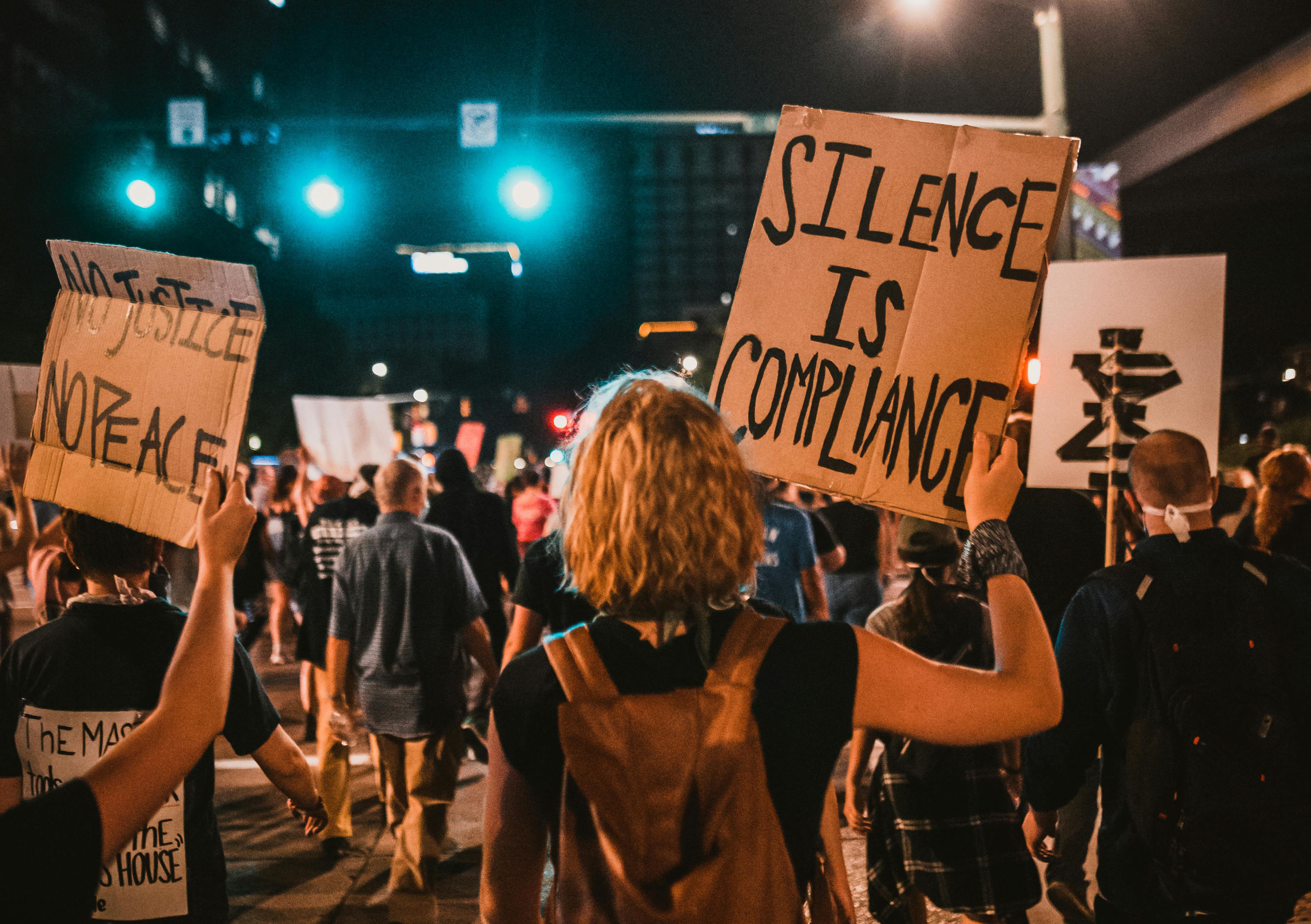 Women's march, photo from back showing sign "Silence is compliance" and "No justice, no peace"