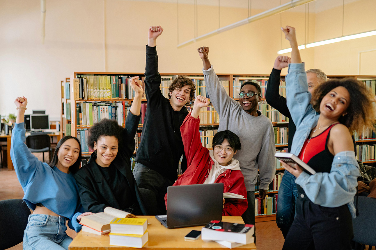 Diverse group of college studentsin library raising they hand in a fist and smiling